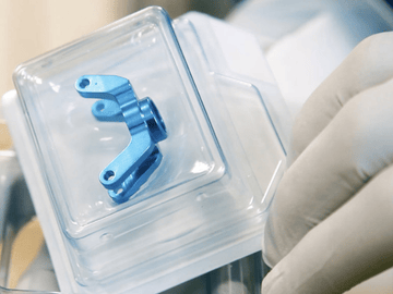 Eine behandschuhte Hand, die ein sicher verpacktes Implantat hält. Das Implantat ist sicher in einem harten Blister verpackt.