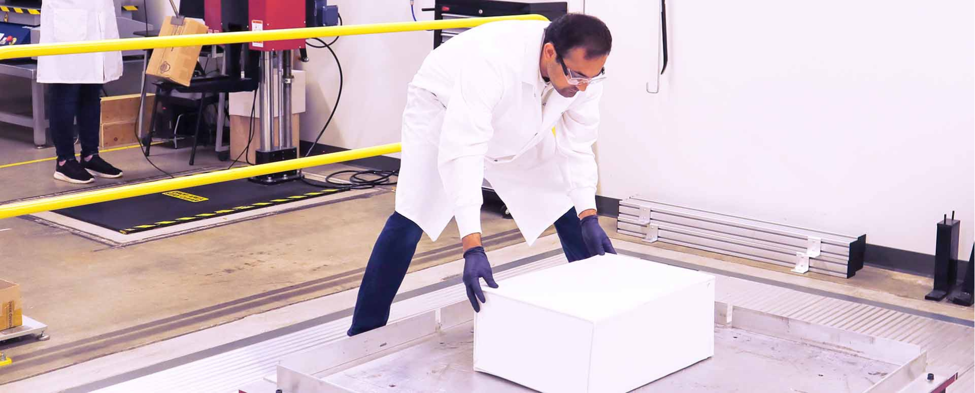 A man in a lab coat places a white box on a vibration table for testing