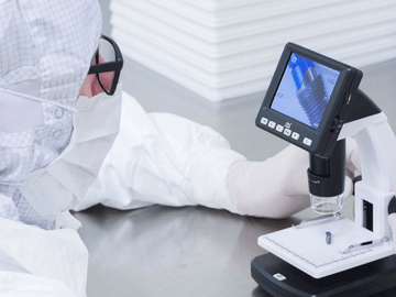 Ein Laborant in einem Reinraum-Overall, der eine chirurgische Maske und Handschuhe trägt, führt einen Test an einer Komponente eines medizinischen Geräts durch. 