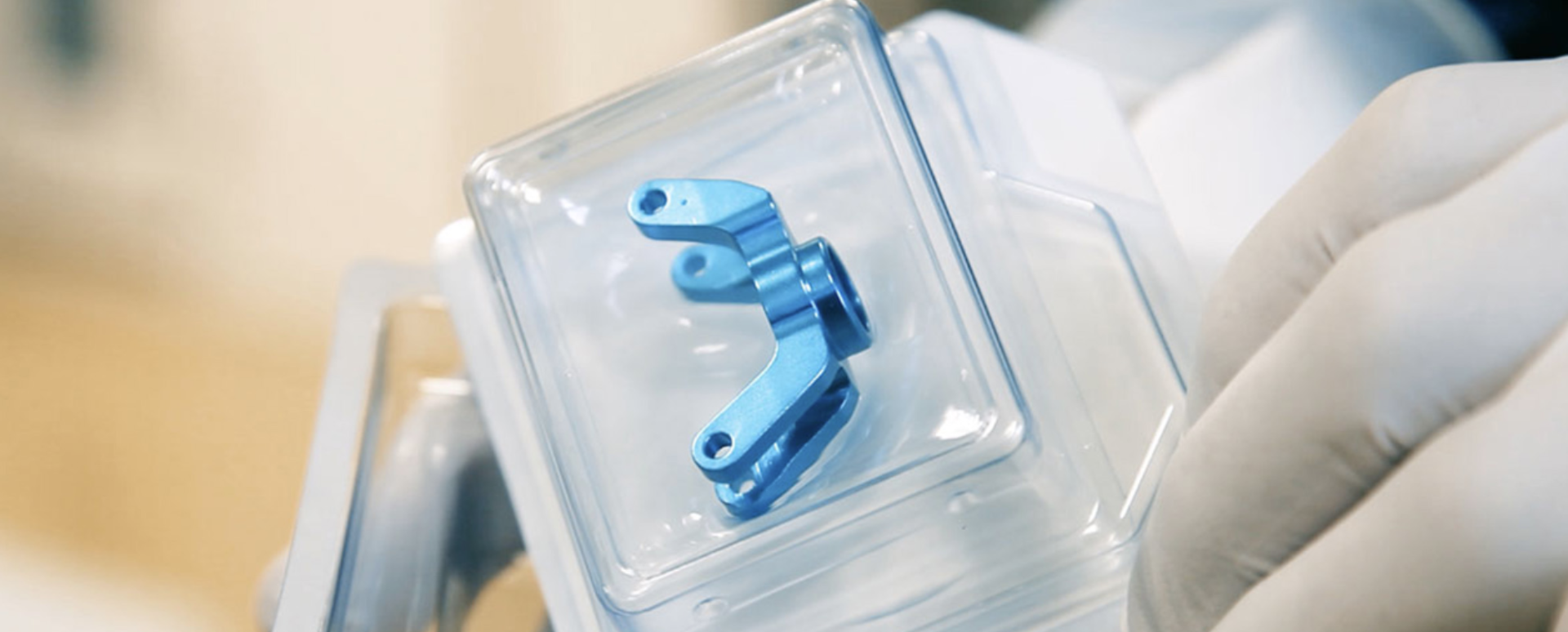 Eine behandschuhte Hand, die ein sicher verpacktes Implantat hält. Das Implantat ist sicher in einem harten Blister verpackt.